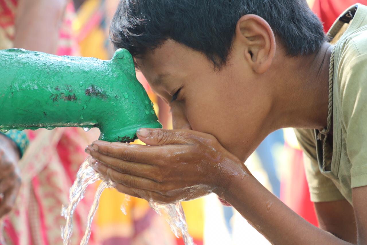 A young boy in Nepal cups his hands under a bright green running tap and and drinks the clean water pooled there. You can see the pleasure in his face as he drinks the cool, fresh water.