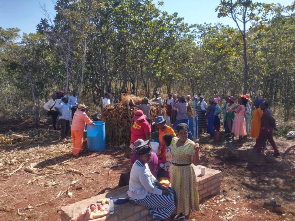 A group of female farmers chat together in the foreground. Behind them, their fellow trainees are loading up a compost heap.