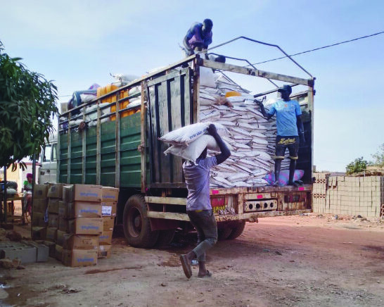 Three men in Burkina Faso load a large open backed lorry with sacks of grain. The road is dusty and bare.